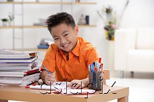 AsiaPix - Boy sitting at desk doing homework, smiling at camera, portrait