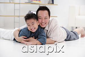AsiaPix - Father and son lying on floor, embracing, portrait