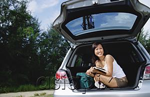 AsiaPix - Woman sitting in boot of car, holding magazine