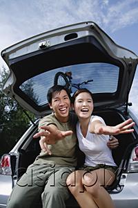 AsiaPix - Couple sitting in boot of car, reaching towards camera
