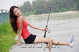 AsiaPix - Woman sitting by river, holding fishing rod