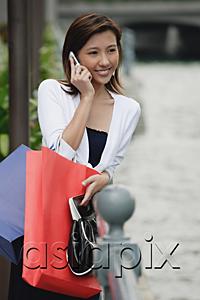 AsiaPix - Woman leaning on railing, carrying shopping bags, using mobile phone