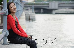 AsiaPix - Woman sitting by river, listening to MP3 player, smiling at camera