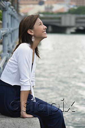 AsiaPix - Woman sitting by river, smiling, looking up