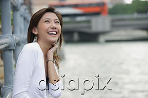 AsiaPix - Woman sitting by river, smiling, looking up