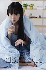 AsiaPix - Young woman on bed, holding glass of water and pills