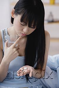 AsiaPix - Young woman holding glass of water and looking at pills in palm of hand