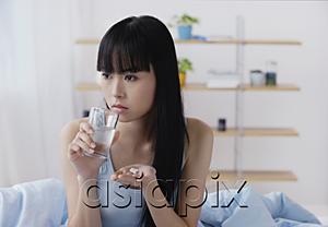 AsiaPix - Young woman holding glass of water and pills, looking away