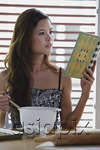 AsiaPix - Young woman in kitchen, looking at cookbook