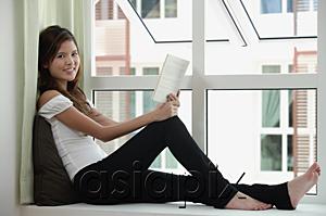 AsiaPix - Woman sitting by window holding a book, smiling at camera
