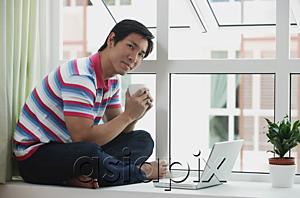 AsiaPix - Man sitting on bay window using laptop
