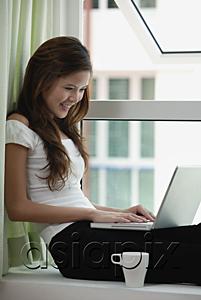 AsiaPix - Woman sitting by window using a laptop