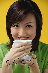 AsiaPix - Young woman drinking from tea cup, smiling at camera