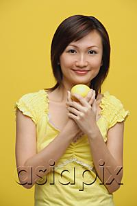 AsiaPix - Young woman holding lemon, standing against yellow background