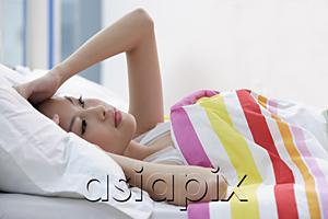 AsiaPix - Young woman lying on bed, looking up, pensive expression