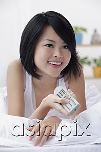 AsiaPix - Young woman lying on bed, holding TV remote control, smiling