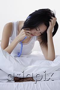 AsiaPix - Young woman sitting on bed, using telephone, hand on head