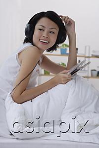 AsiaPix - Young woman sitting on bed, listening to music