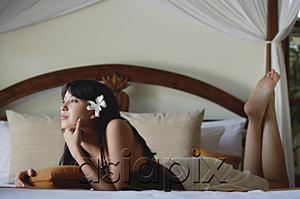 AsiaPix - Young woman lying on bed, hand on chin, looking away