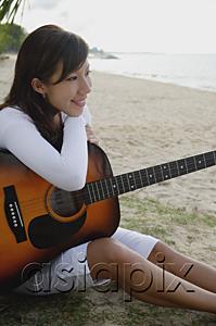 AsiaPix - Young woman sitting on beach, leaning on guitar
