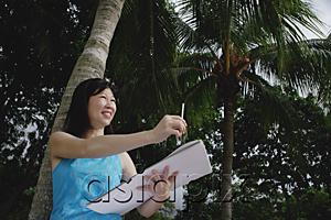 AsiaPix - Woman with sketchbook standing under a coconut tree