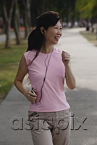 AsiaPix - Mature woman walking in park, listening to MP3 player, smiling