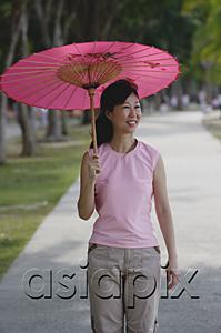 AsiaPix - Mature woman walking in park, using pink umbrella