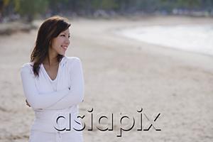 AsiaPix - Young woman standing on beach, arms crossed, looking away