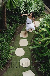 AsiaPix - Young woman walking in tropical garden, smiling at camera
