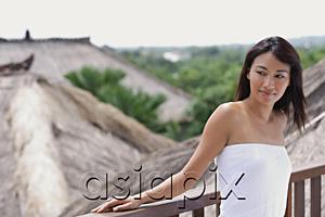 AsiaPix - Young woman leaning on railing looking away, thatched roofs behind her