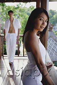 AsiaPix - Young woman in balcony looking at camera, man standing in background