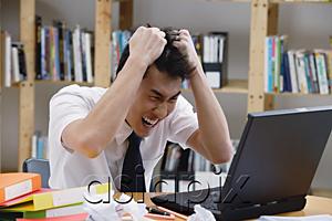 AsiaPix - Young man in library, pulling his hair, looking at laptop