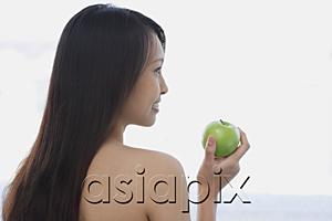 AsiaPix - Young woman holding green apple, looking away