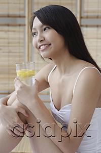 AsiaPix - Young woman holding glass of water, hugging knees, looking away