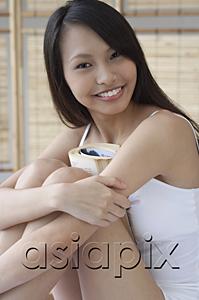 AsiaPix - Young woman hugging knees, smiling at camera
