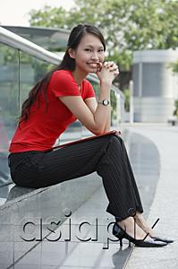 AsiaPix - Young woman sitting on ledge outdoors, smiling at camera