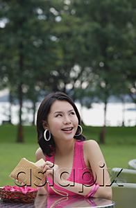 AsiaPix - Young woman sitting at outdoor table, holding wallet, looking away