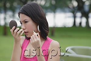 AsiaPix - Young woman outdoors, looking at compact, applying make-up
