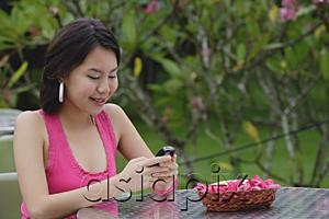 AsiaPix - Young woman sitting at outdoor table, looking at mobile phone