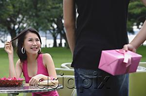 AsiaPix - Woman seated at table, man in foreground holding gift behind his back