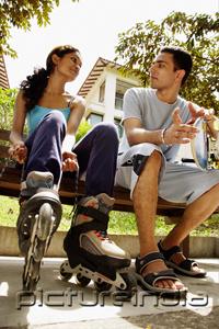 PictureIndia - Man and woman on bench side by side, woman lacing up roller blades