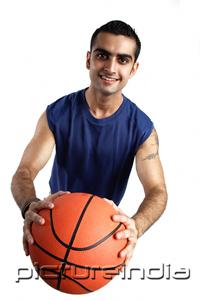 PictureIndia - Young man holding basketball forward, looking at camera