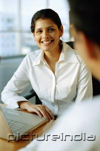 PictureIndia - Female executive smiling at man facing her, over the shoulder view