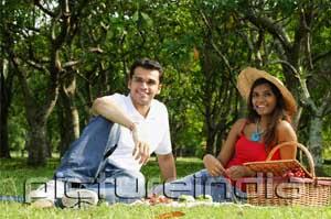 PictureIndia - Couple in park, sitting on grass, having picnic, looking at camera