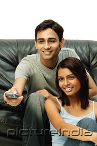 PictureIndia - Couple sitting and facing forward, man holding remote control