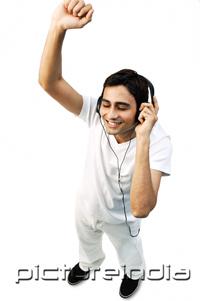 PictureIndia - Young man listening to headphones, eyes closed, arms raised