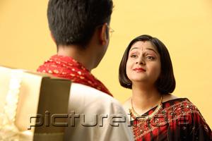 PictureIndia - Indian couple standing face to face, man hiding gift behind back