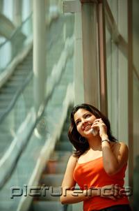 PictureIndia - Woman leaning in glass wall using mobile phone, smiling