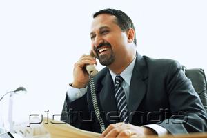 PictureIndia - Businessman using telephone in office, smiling
