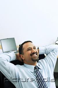 PictureIndia - Businessman in office, hands behind head, smiling